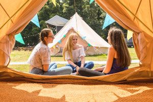 Three friends sat in front of a yurt with colourful bunting.